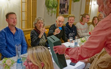 Verschiedene grüne Mitglieder sitzen an einem Tisch während eine Box für die Wahl der Delegierten durchgeht.