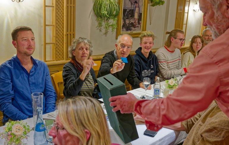 Verschiedene grüne Mitglieder sitzen an einem Tisch während eine Box für die Wahl der Delegierten durchgeht.