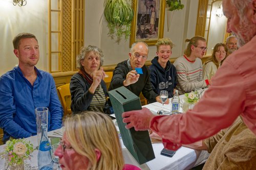 Verschiedene grüne Mitglieder sitzen an einem Tisch während eine Box für die Wahl der Delegierten durchgeht.